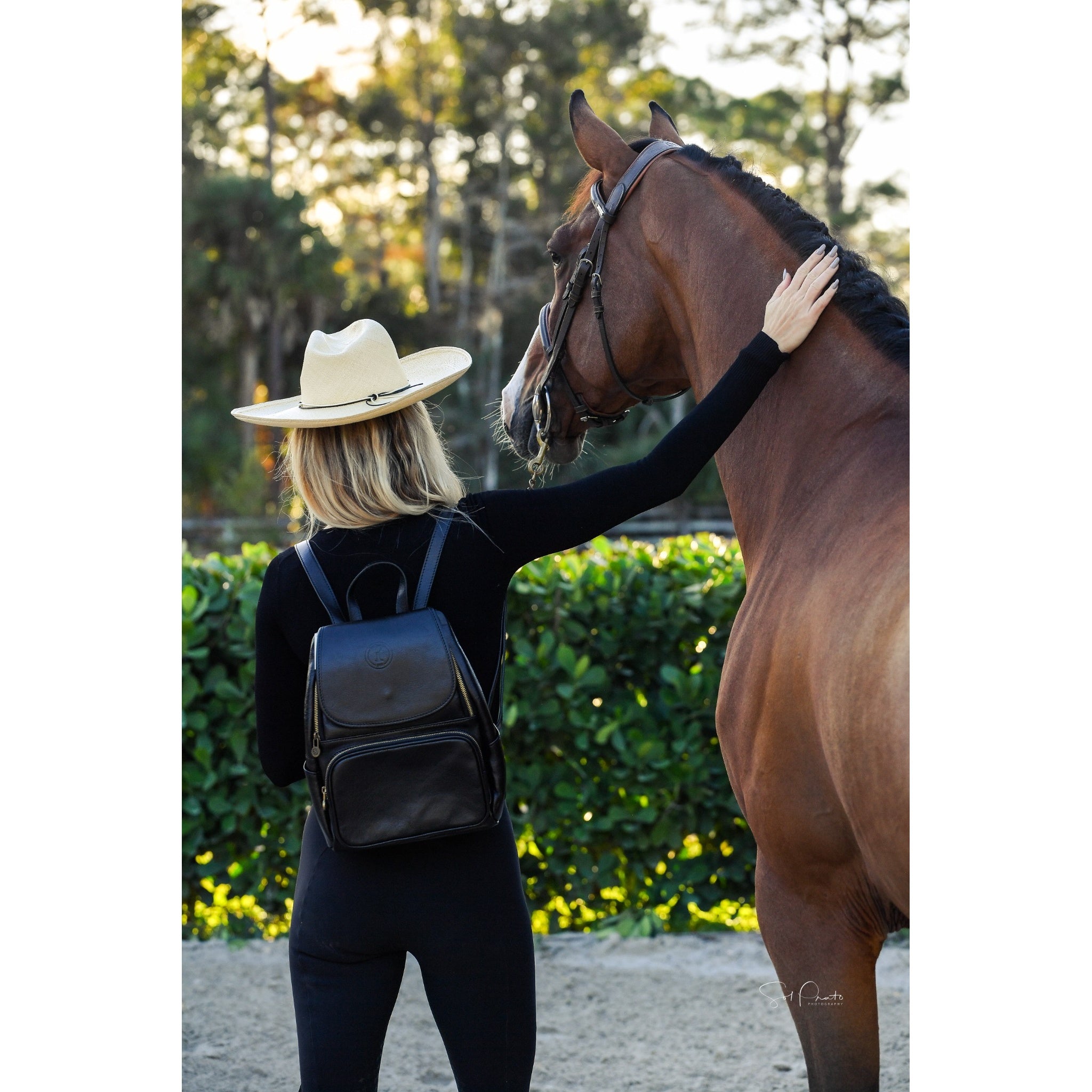 Woman with a black leather backpack and a horse, in an equestrian outdoor setting